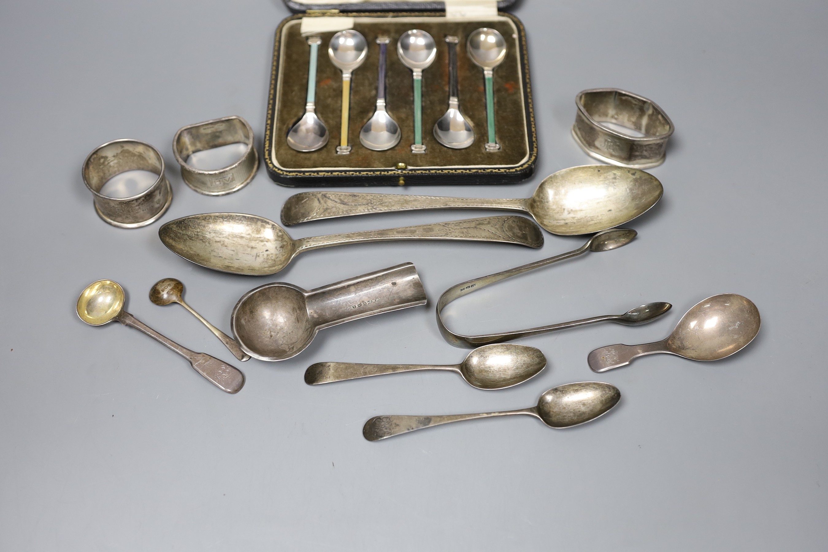 A pair of George III bright cut silver table spoons, three later assorted napkin rings, a cigar stand, a pair of tongs, five assorted spoons, 10oz., and a cased set of silver and enamel coffee spoons